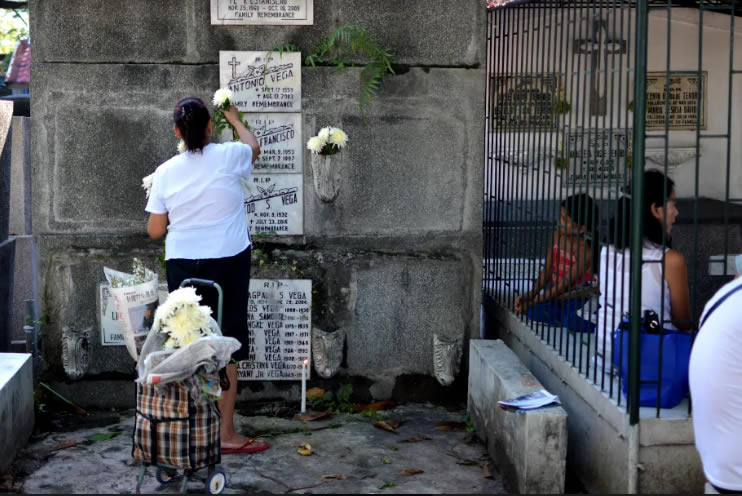 A lady offers flowers on the vases planted beside the tombstone of a loved one as a child from a neighboring mausoleum watches her.(NICEFORO BALBEDINA/CBCPNEWS)